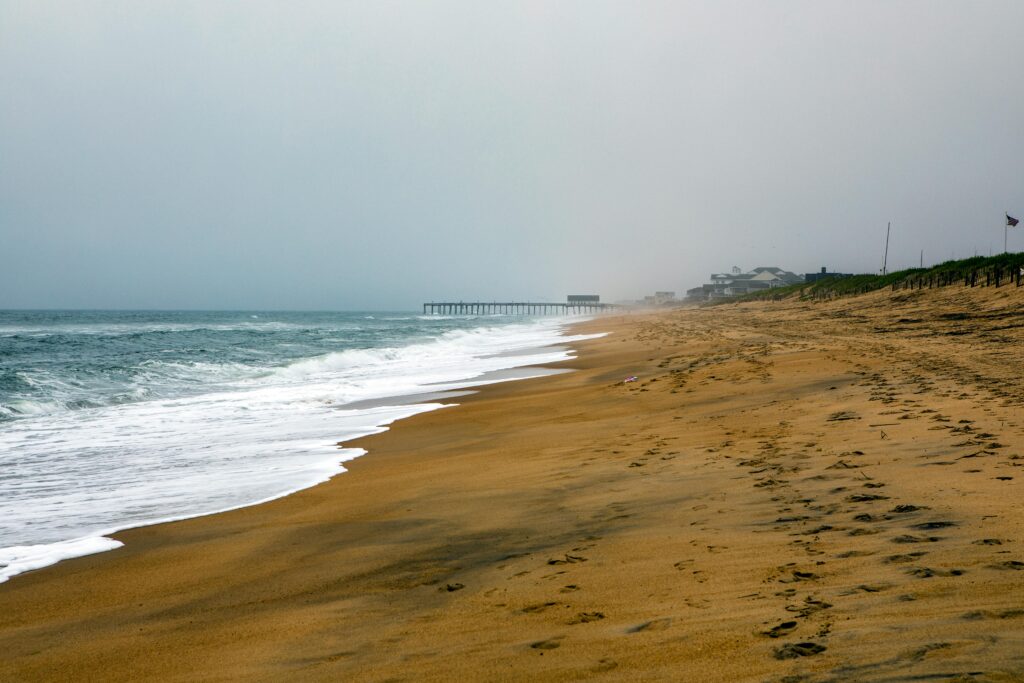 Serene view of Nags Head beach with gentle waves and a distant pier, ideal for relaxation.